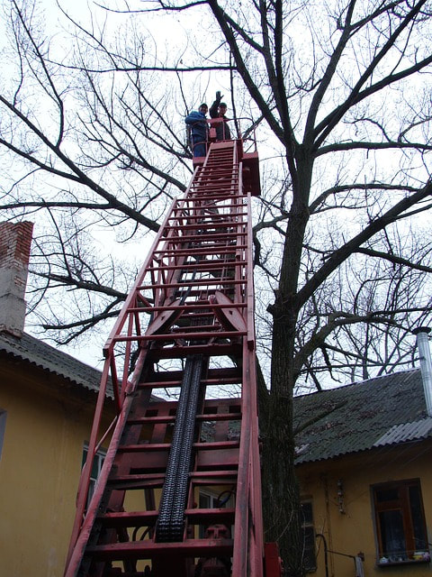 A tree crew using a crane to remove a tree that has fallen on a hosue